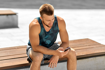 Image showing man with smartphone sitting on bench outdoors