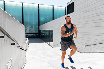 Image showing young man in headphones running upstairs outdoors