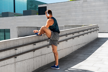 Image showing young man in headphones stretching leg outdoors