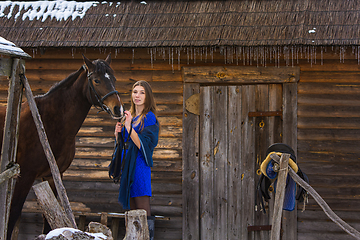 Image showing A girl stands with a horse against the background of an old wooden house