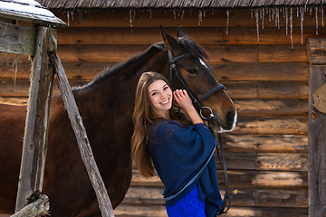 Image showing Portrait of a girl hugging a horse against the background of a wall of logs