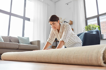 Image showing young woman unfolding carpet at home