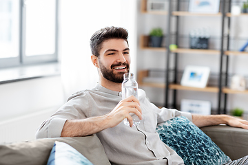 Image showing happy man drinking water from glass bottle at home