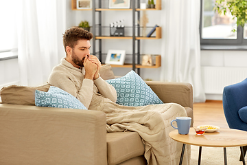 Image showing sick young man in blanket with hot tea at home