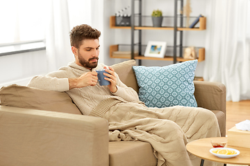 Image showing sick young man in blanket drinking hot tea at home