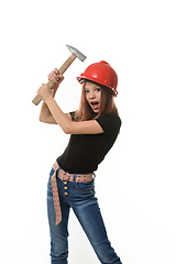 Image showing A girl in a hard hat hits herself on the head with a hammer, surprise on her face