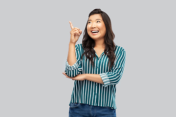 Image showing happy asian woman pointing finger up on grey