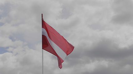 Image showing Latvia flag on the flagpole waving in the wind against a blue sky with clouds. Slow motion