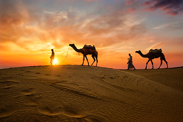 Image showing Indian cameleers camel driver with camel silhouettes in dunes on sunset. Jaisalmer, Rajasthan, India