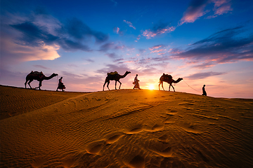 Image showing Indian cameleers camel driver with camel silhouettes in dunes on sunset. Jaisalmer, Rajasthan, India