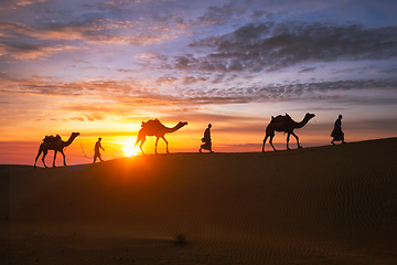 Image showing Indian cameleers camel driver with camel silhouettes in dunes on sunset. Jaisalmer, Rajasthan, India