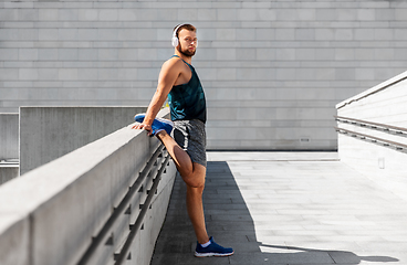 Image showing young man in headphones stretching leg outdoors