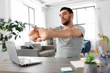 Image showing man with laptop stretching at home office