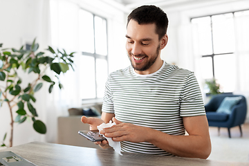 Image showing man cleaning phone with wet wipe at home office