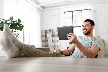 Image showing man with tablet pc resting feet on table at home