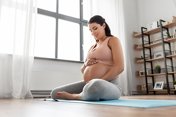 Image showing happy pregnant woman sitting on yoga mat at home