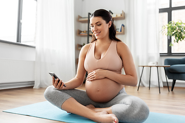 Image showing happy pregnant woman with phone doing yoga at home