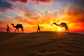 Image showing Indian cameleers camel driver with camel silhouettes in dunes on sunset. Jaisalmer, Rajasthan, India