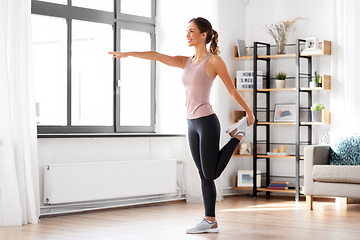 Image showing smiling young woman stretching leg at home