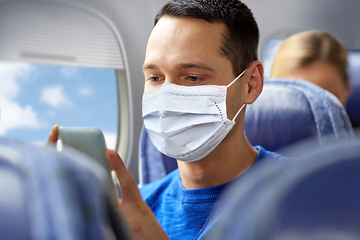 Image showing man in mask sitting in plane with smartphone