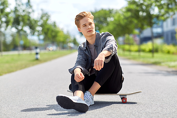 Image showing teenage boy sitting on skateboard on city street
