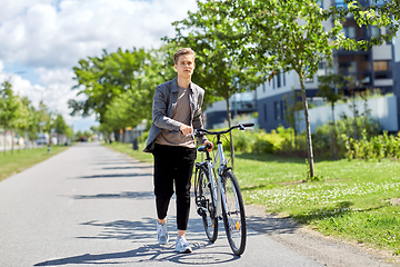 Image showing young man with bicycle walking along city street