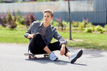 Image showing teenage boy sitting on skateboard on city street