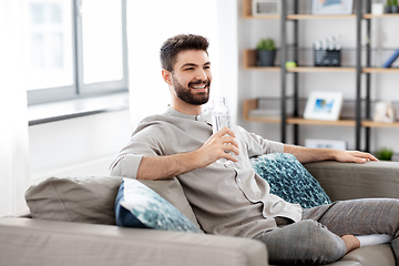 Image showing happy man drinking water from glass bottle at home