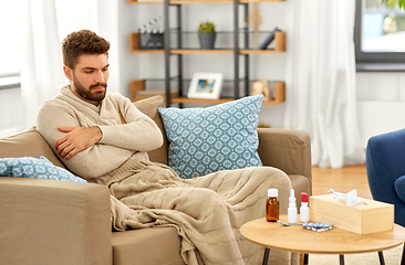 Image showing sad sick man in blanket with medicine at home