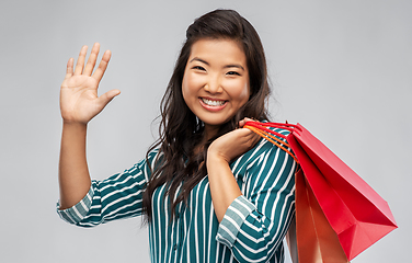 Image showing happy asian woman with shopping bags waving hand