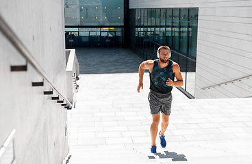 Image showing young man in headphones running upstairs outdoors