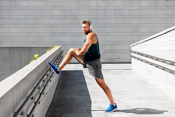 Image showing young man in headphones stretching leg outdoors