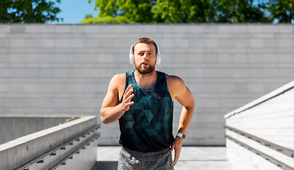 Image showing young man in headphones running outdoors