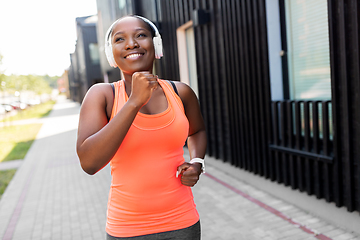 Image showing happy african woman in headphones running outdoors