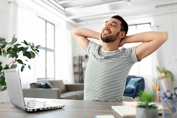 Image showing happy man with laptop stretching at home office