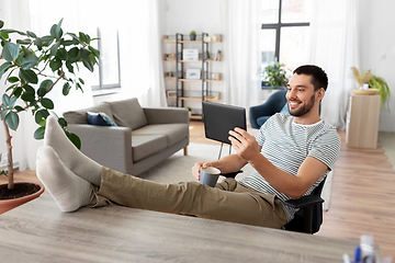 Image showing man with tablet pc resting feet on table at home