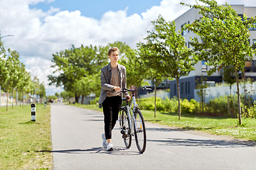 Image showing young man with bicycle walking along city street