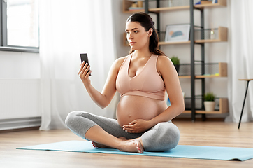 Image showing pregnant woman with smartphone exercising at home