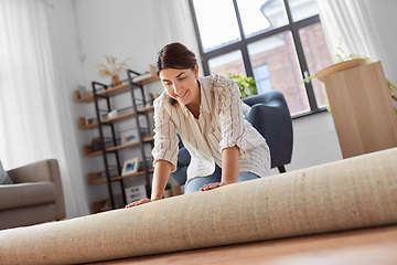 Image showing young woman unfolding carpet at home