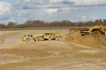 Image showing Yellow dump trucks and excavator are working in gravel pit