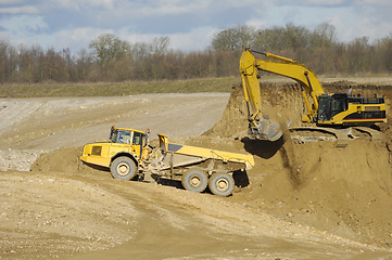 Image showing Yellow dump trucks and excavator are working in gravel pit