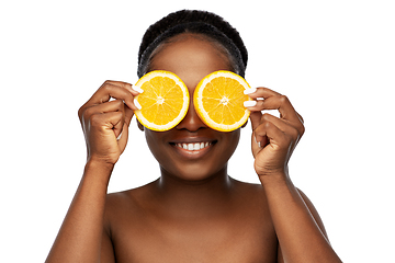 Image showing smiling african woman making eye mask of oranges