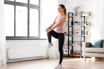 Image showing smiling young woman stretching leg at home