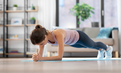 Image showing young woman doing plank exercise on mat at home