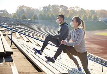 Image showing couple in masks stretching leg on stadium