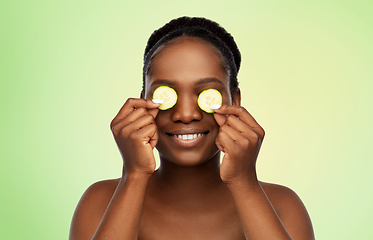 Image showing happy african woman making eye mask of cucumbers