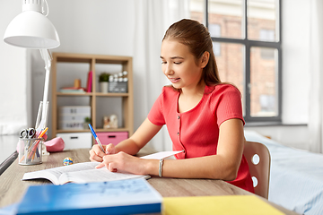 Image showing student girl with book writing to notebook at home