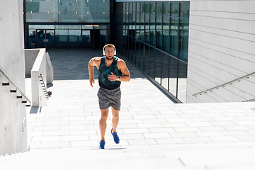 Image showing young man in headphones running upstairs outdoors