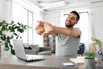 Image showing happy man with laptop stretching at home office