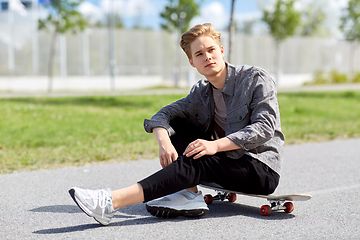 Image showing teenage boy sitting on skateboard on city street